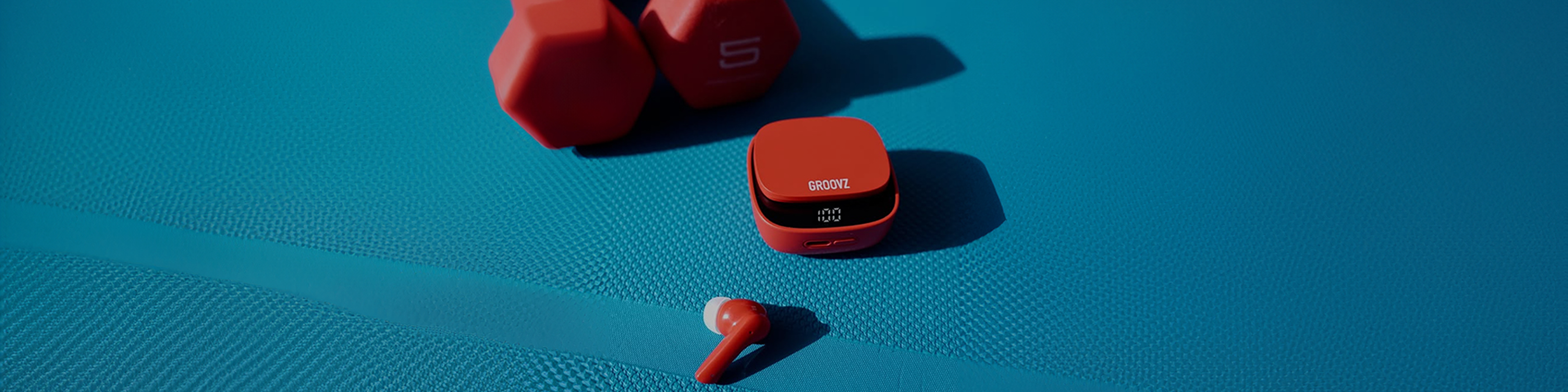 Groovz True Wireless Earbuds in Red with LED Charging Case – Shown on Blue Yoga Mat Next to Dumbbells for Active Lifestyle Use