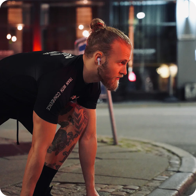 Athletic Man Wearing Groovz Wireless Earbuds in White While Preparing for Night Run – Outdoor Urban Fitness Scene with Tattoos and Training Gear