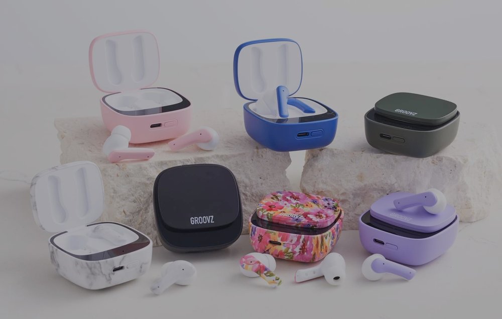 a display of Groovz wireless earbuds with colorful charging cases in pink, blue, black, green, white marble, floral, and purple.